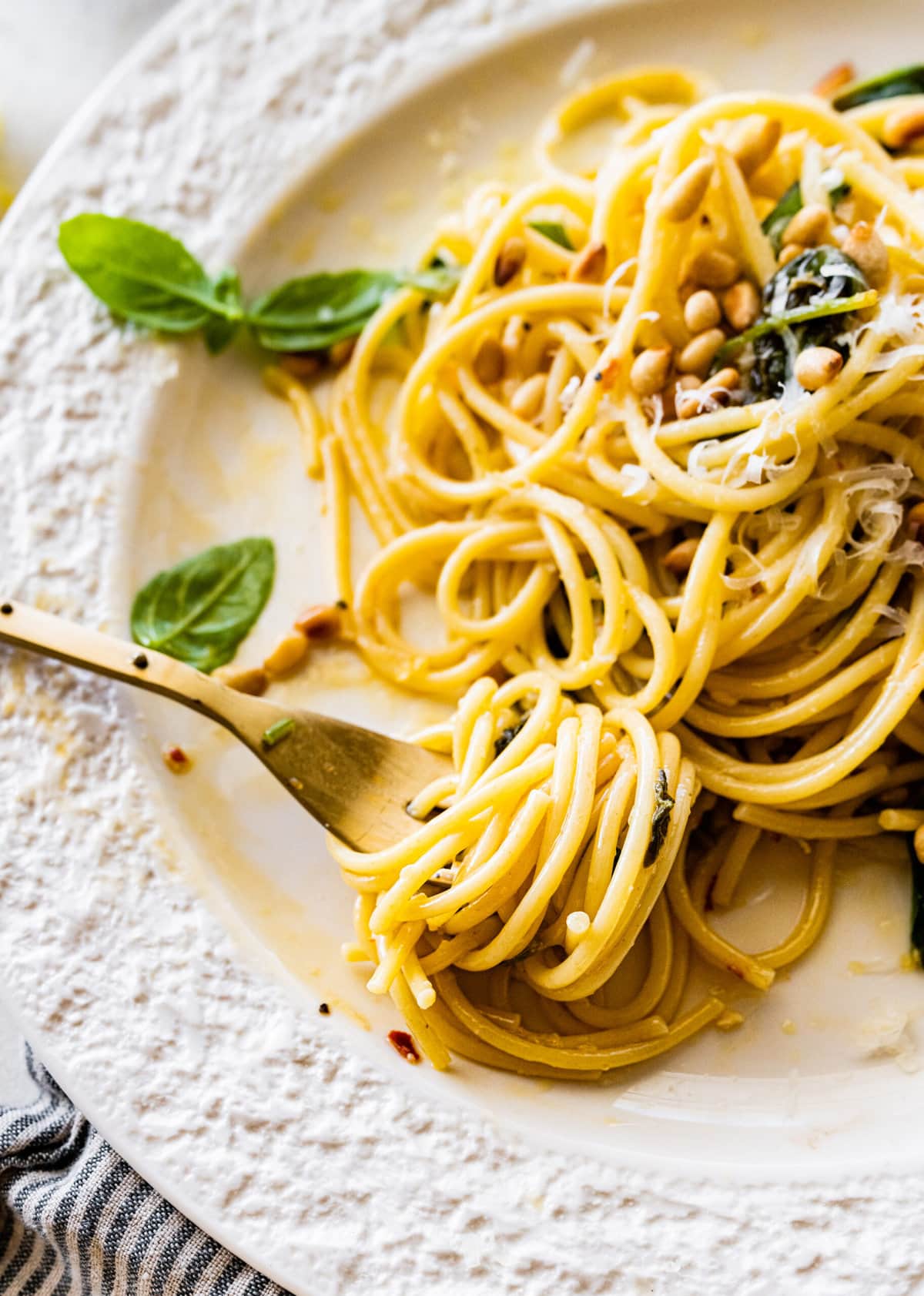 a plate with a portion of Easy Pasta with Sautéed Spinach and Garlic toasted pine nuts on top. Fork with a twirl of spaghetti around it.