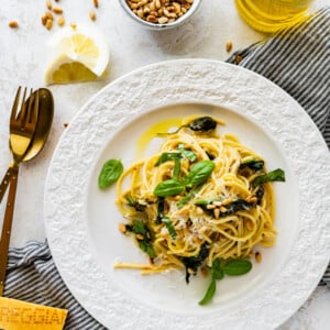 a plate with a portion of Easy Pasta with Sautéed Spinach and Garlic toasted pine nuts on top. Fork and spoon near plate.