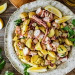 Italian Octopus Salad Recipe with Potatoes (Insalata Di Polpo) in a large round serving platter. Side of lemon, parley on top, and bread as a side.