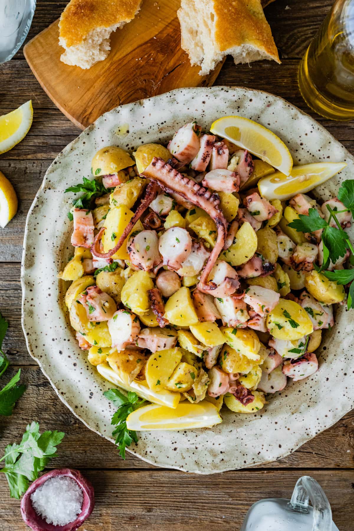 Italian Octopus Salad Recipe with Potatoes (Insalata Di Polpo) in a large round serving platter. Side of lemon, parley on top, and bread as a side. 
