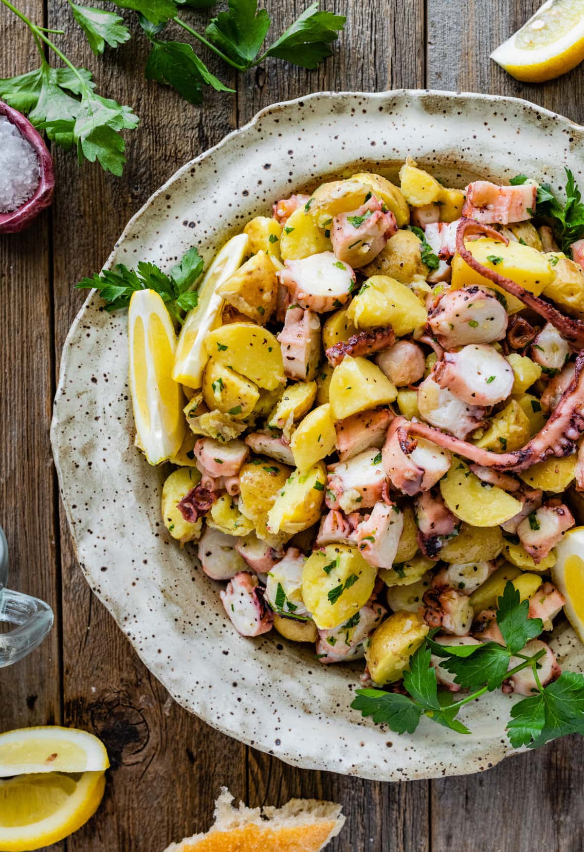 Italian Octopus Salad Recipe with Potatoes (Insalata Di Polpo) in a large round serving platter. Side of lemon, parley on top, and bread as a side.