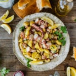 Italian Octopus Salad Recipe with Potatoes (Insalata Di Polpo) in a large round serving platter. Side of lemon, parley on top, and bread as a side.