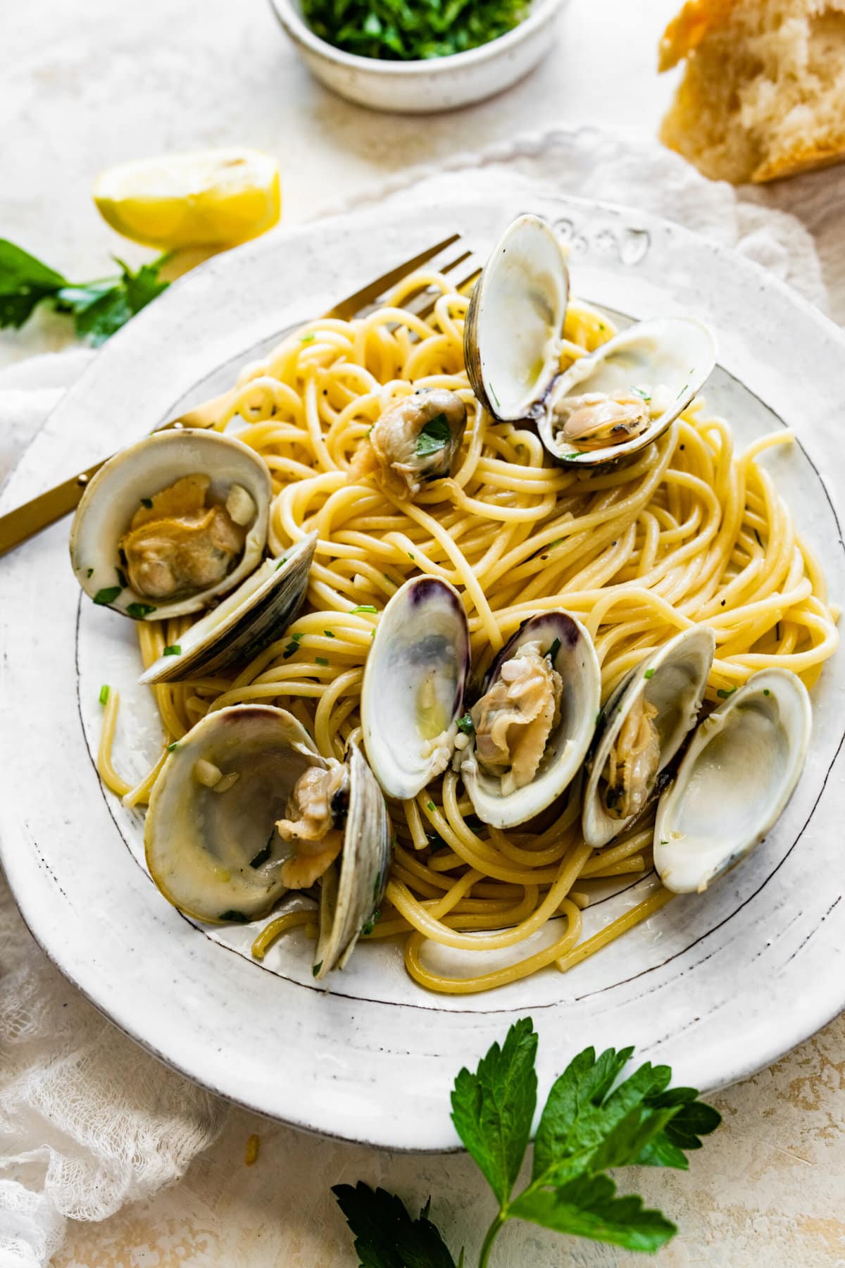 Spaghetti alle Vongole Recipe (Pasta with Clams)- on a plate with a fork. Fresh parsley and lemon as garnish.