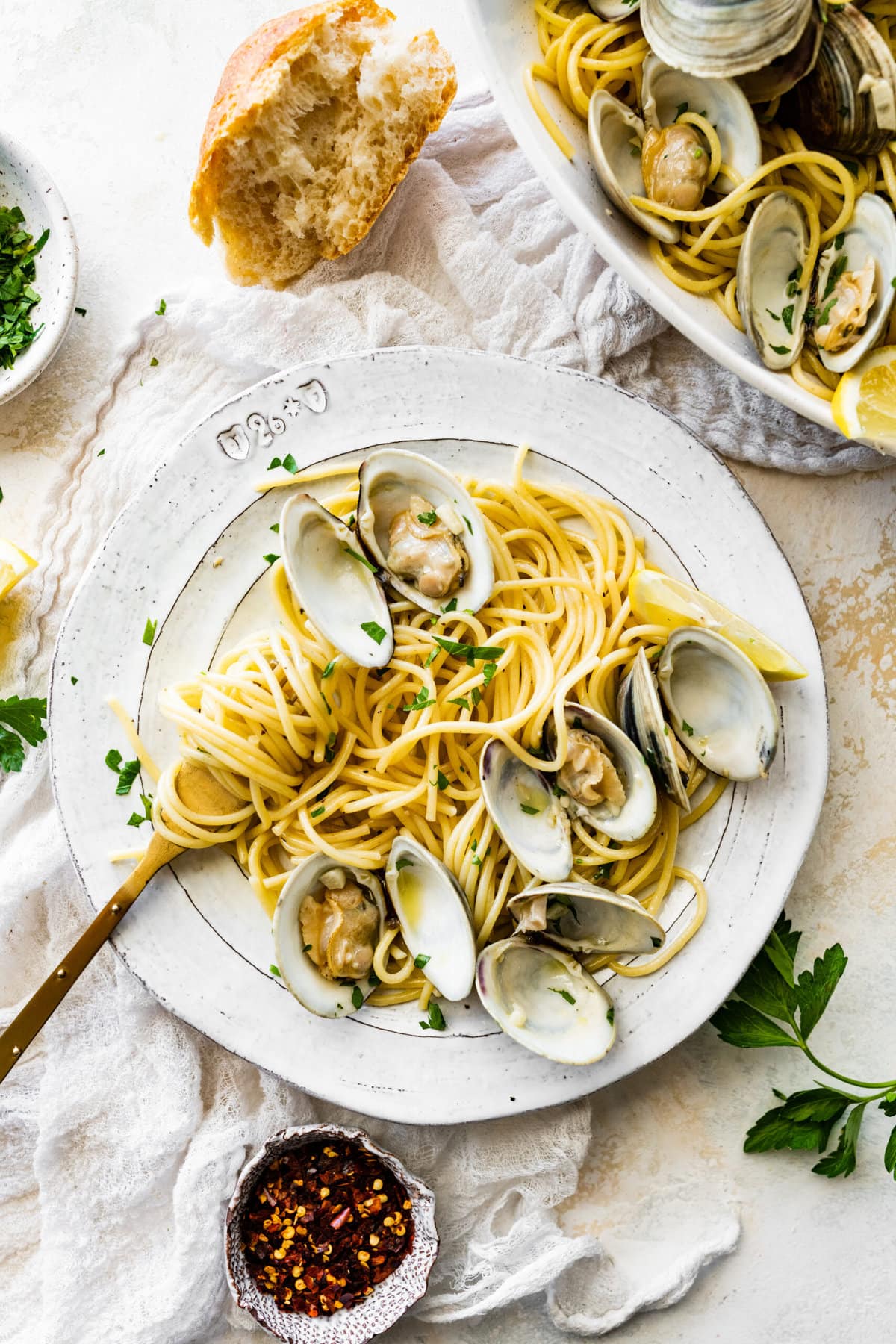 Spaghetti alle Vongole Recipe (Pasta with Clams)- on a plate with a fork. Fresh parsley and lemon as garnish. Fork is twirling the spaghetti on a fork.