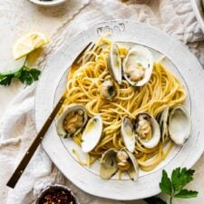 Cover photo. Spaghetti alle Vongole Recipe (Pasta with Clams)- on a plate with a fork. Fresh parsley and lemon as garnish.