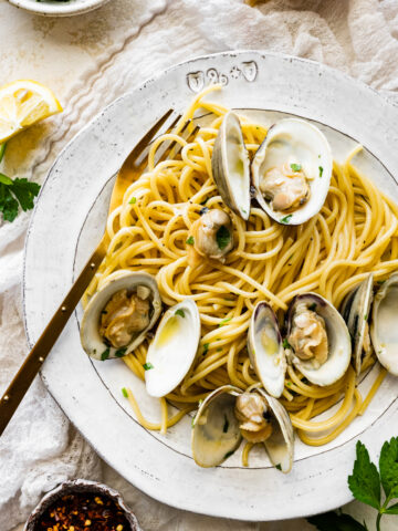 Cover photo. Spaghetti alle Vongole Recipe (Pasta with Clams)- on a plate with a fork. Fresh parsley and lemon as garnish.