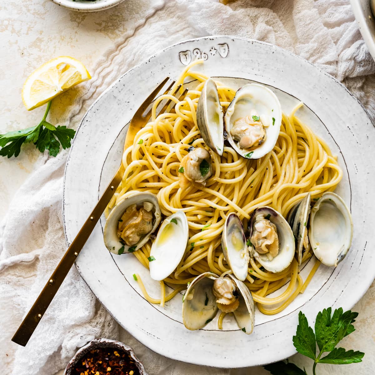 Spaghetti alle Vongole Recipe (Pasta with Clams)- on a plate with a fork. Fresh parsley and lemon as garnish.