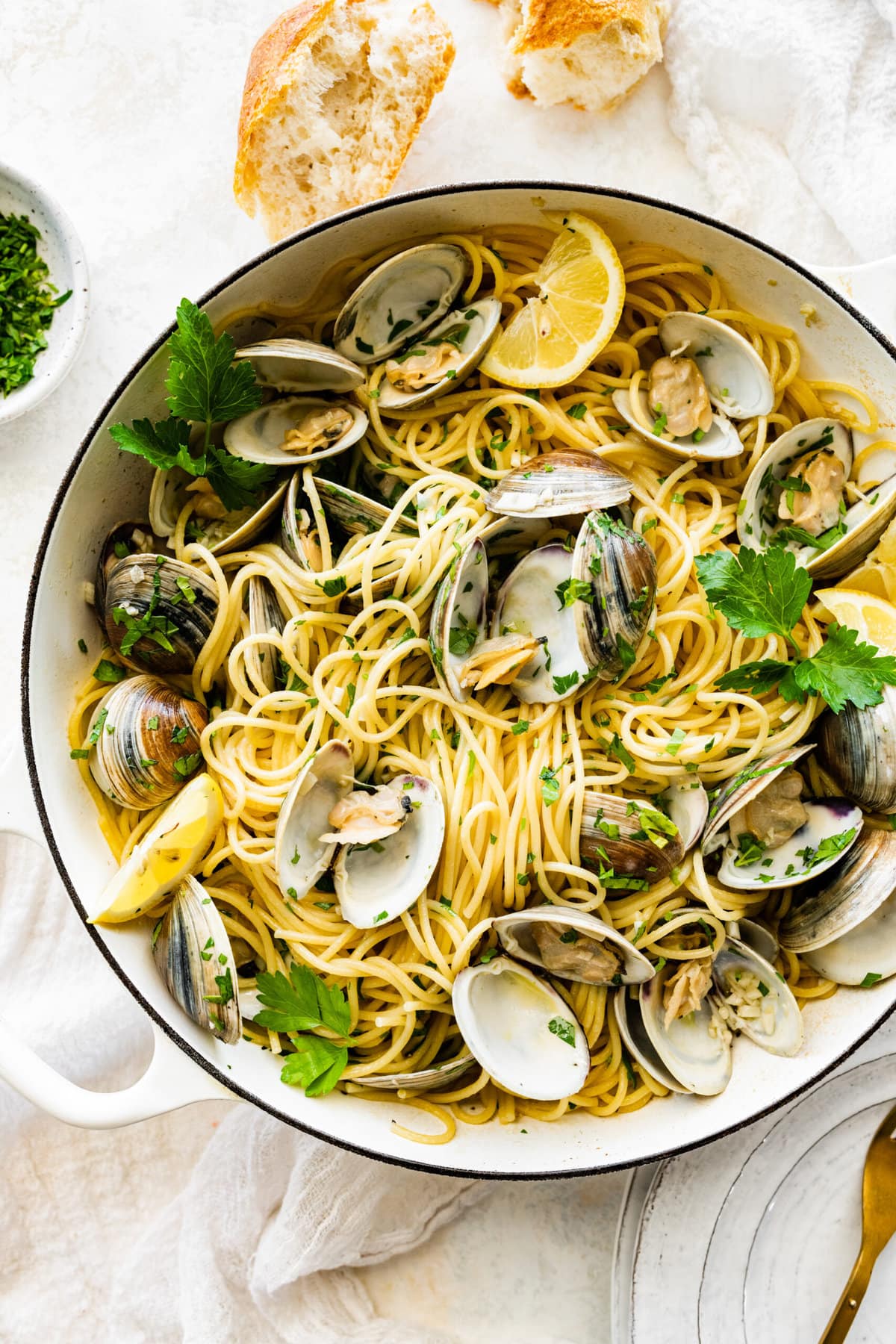 Spaghetti alle Vongole Recipe in the pan with bread and fresh parsley surrounding the white pan.