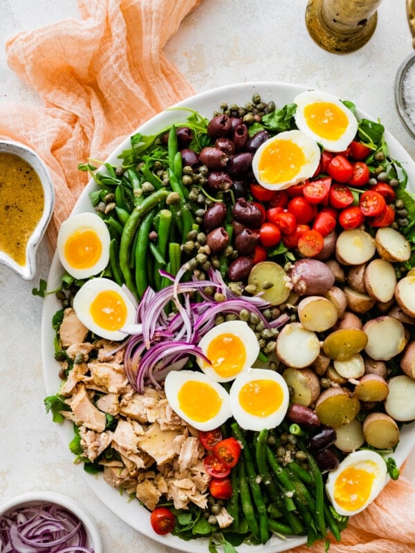 salad in a large serving platter with serving ware and vinaigrette on the side. Cover image.