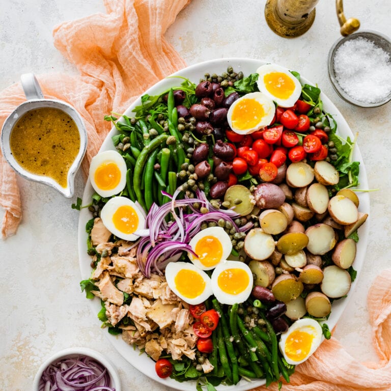 salad in a large serving platter with serving ware and vinaigrette on the side. Cover image.