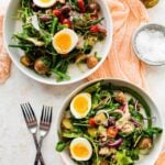 Salad served in two serving bowls with forks and bread on the side.