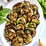 Easy Italian Grilled Eggplant Recipe (Melanzane grigliate) on a serving platter with bread slices around it and parsley and basil.