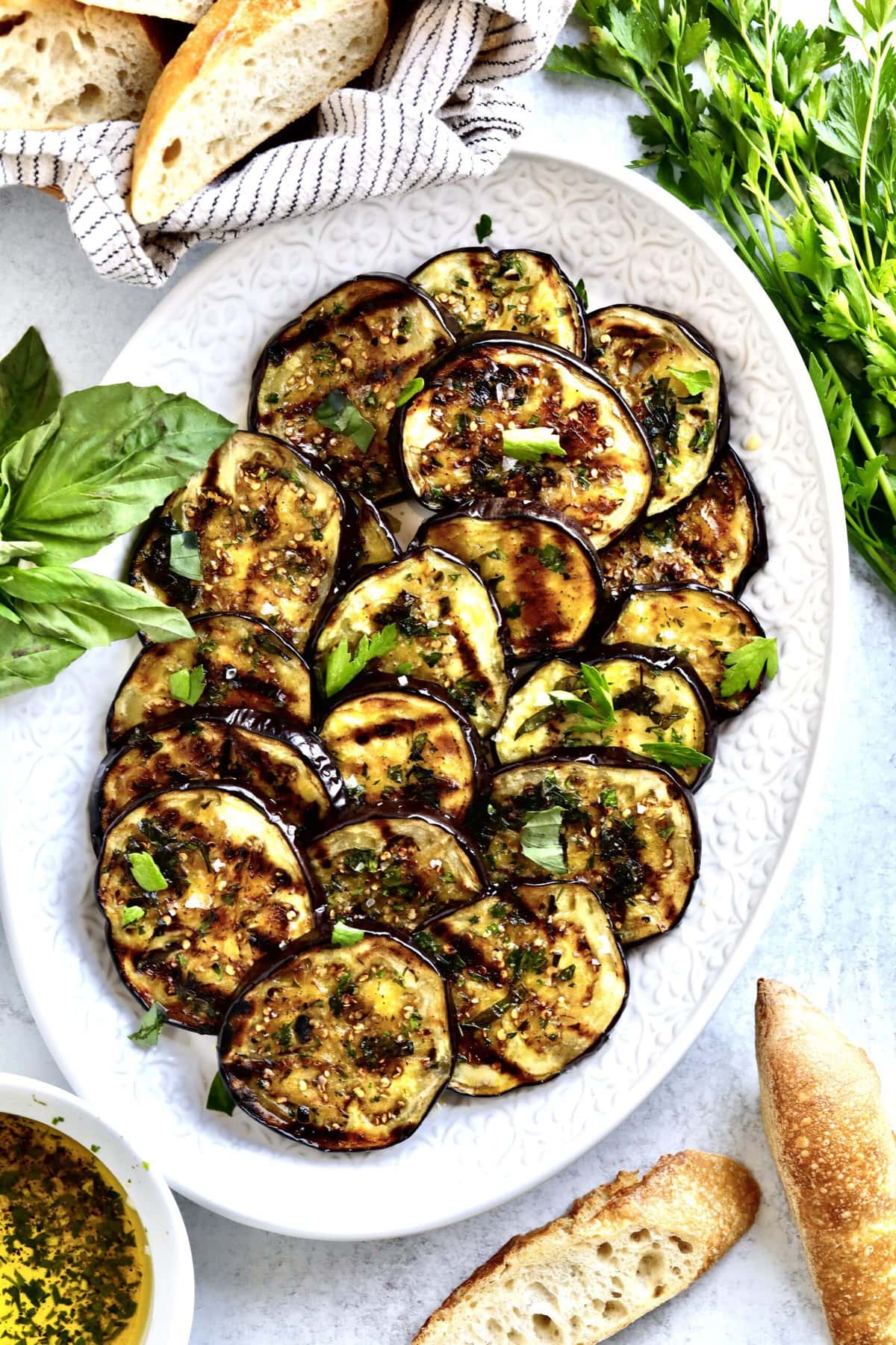 Easy Italian Grilled Eggplant Recipe (Melanzane grigliate) on a serving platter with bread slices around it and parsley and basil.