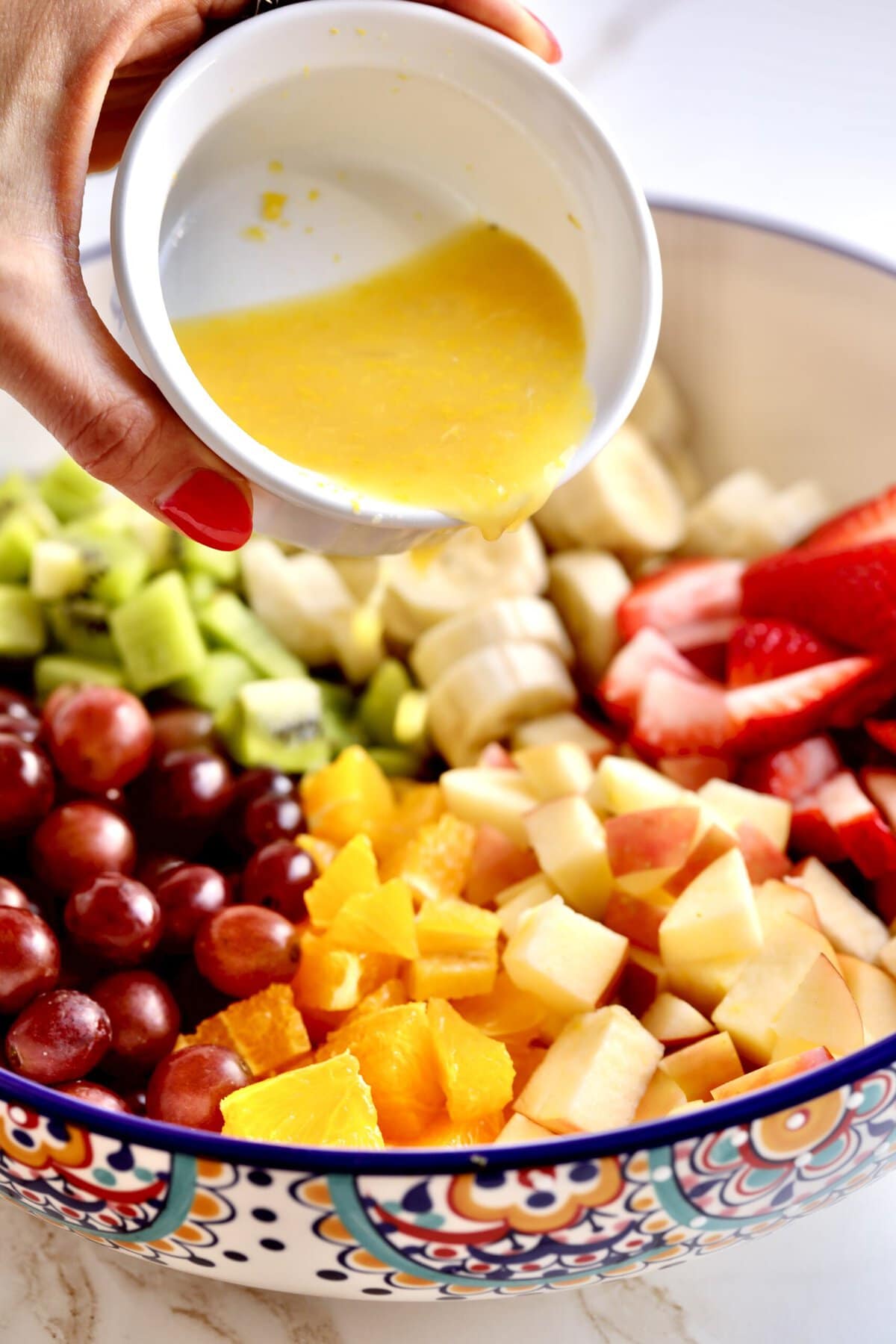 How to make Italian fruit salad recipe- adding the marinade to the fruit in the bowl.