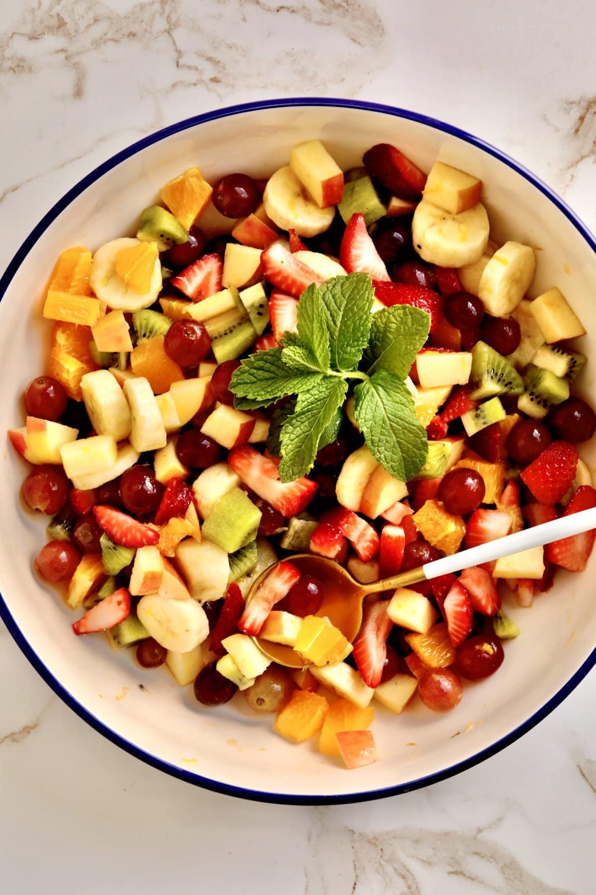 Italian Fruit Salad in a large serving bowl. mint as decoration and large serving spoon int he bowl.