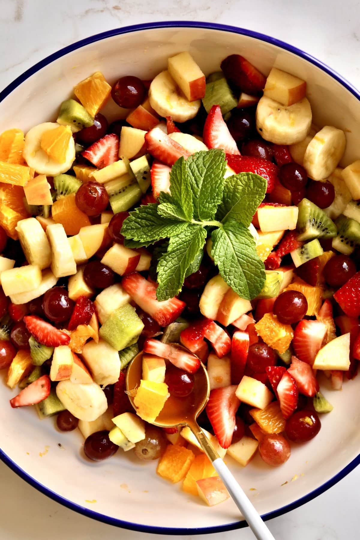 Italian Fruit Salad in a large serving bowl. mint as decoration and large serving spoon int he bowl. 