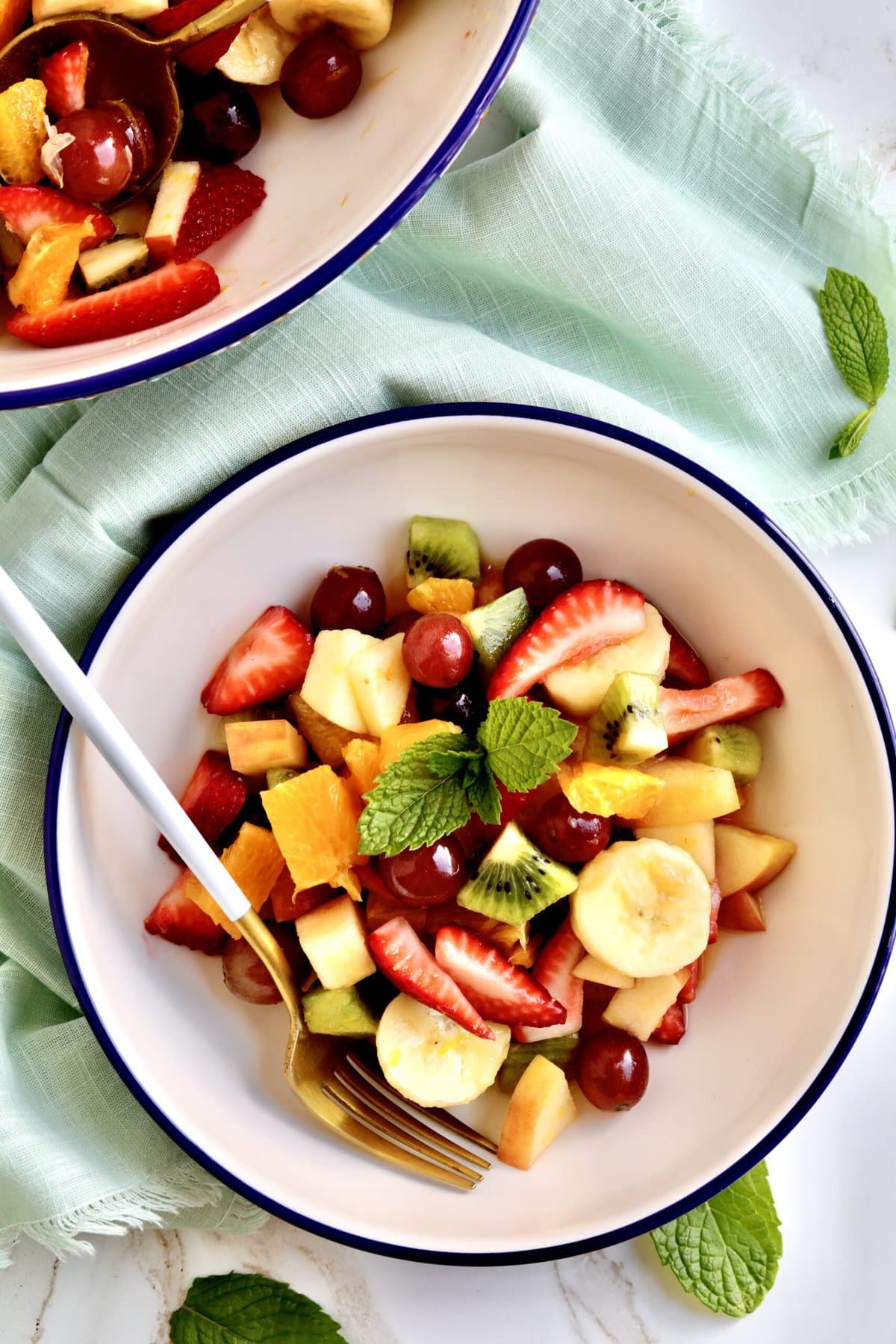 Italian Fruit Salad Recipe (Macedonia di Frutta)- in a bowl with a fork in it ready to eat. Big bowl of fruit salad in background.
