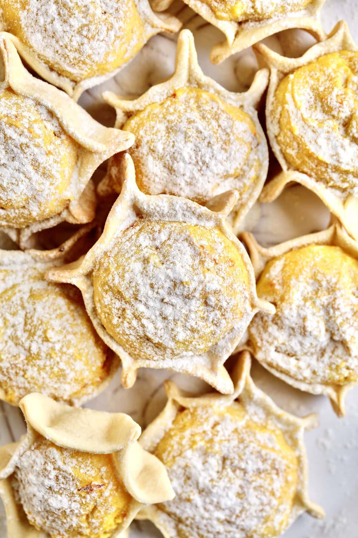 Best Sardinian Pardulas Recipe (Ricotta Cakes)- close up of baked pardulas with powdered sugar. 
