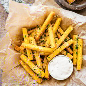 Crispy baked parmesan herb polenta fries on paper with dip.