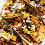 Homemade Tacos Al Pastor Recipe (Tacos De Trompo)- assembled tacos on a plate ready to eat. Limes and parsley on the side.