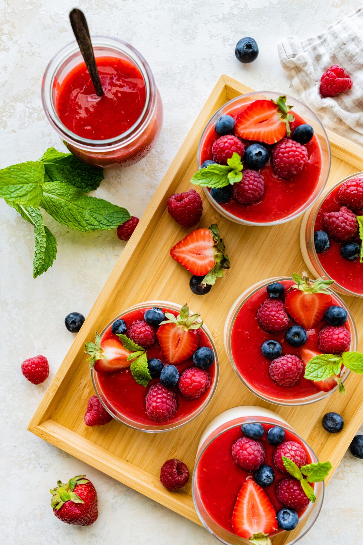 Panna cotta cups with berry puree and berries on a tray. Fresh mint to decorate.