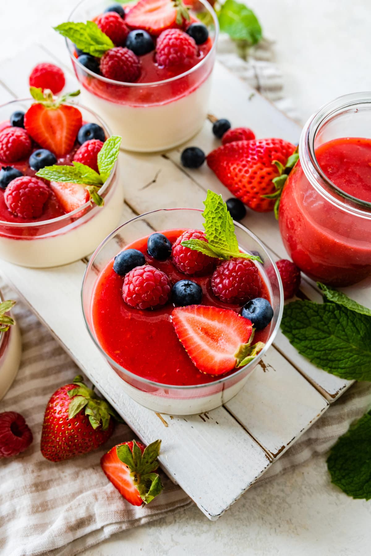 side view of panna cotta and berries in a glass cup to se layers. fresh berries as decoration. Set on wooden tray.