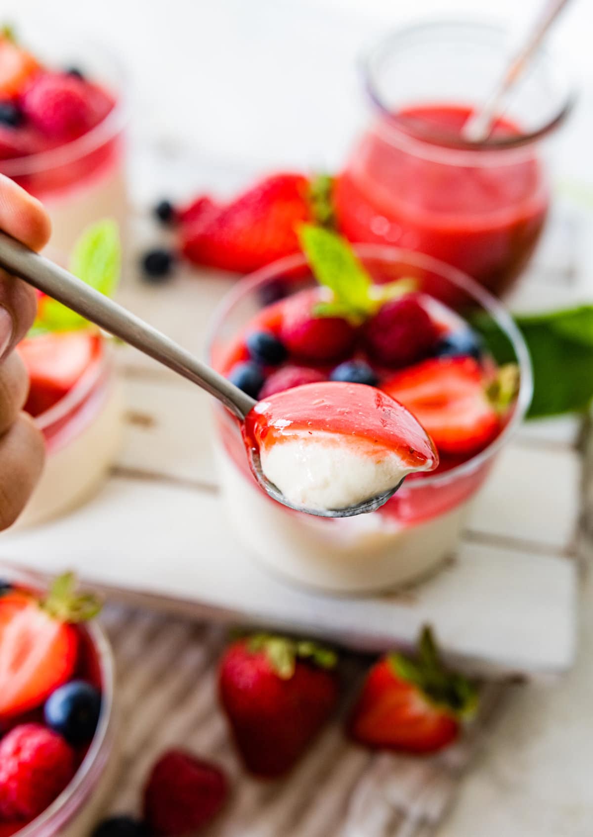 side view of panna cotta and berries in a glass cup to se layers. fresh berries as decoration. Bite taken out of the panna cotta on spoon.