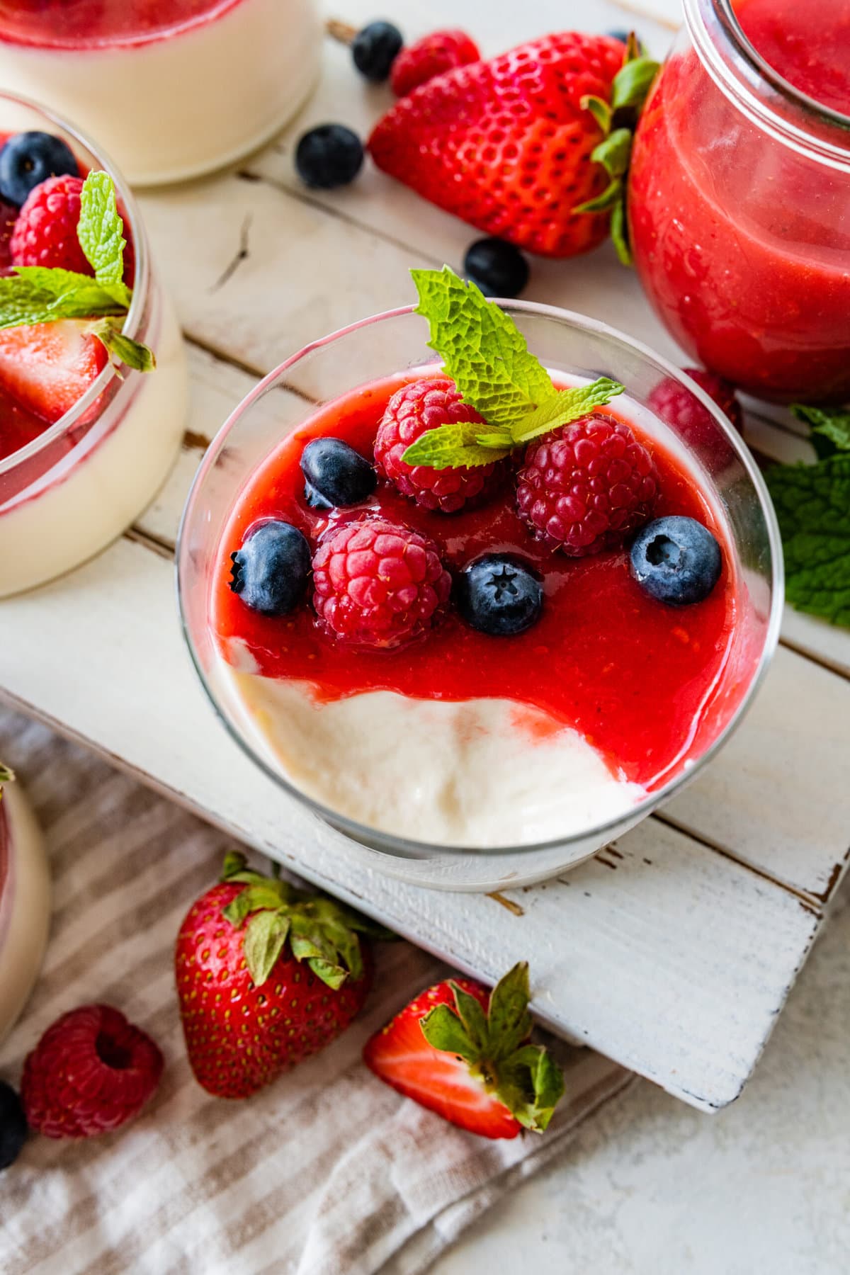 side view of panna cotta and berries in a glass cup to se layers. fresh berries as decoration. Bite taken out of the panna cotta on spoon.