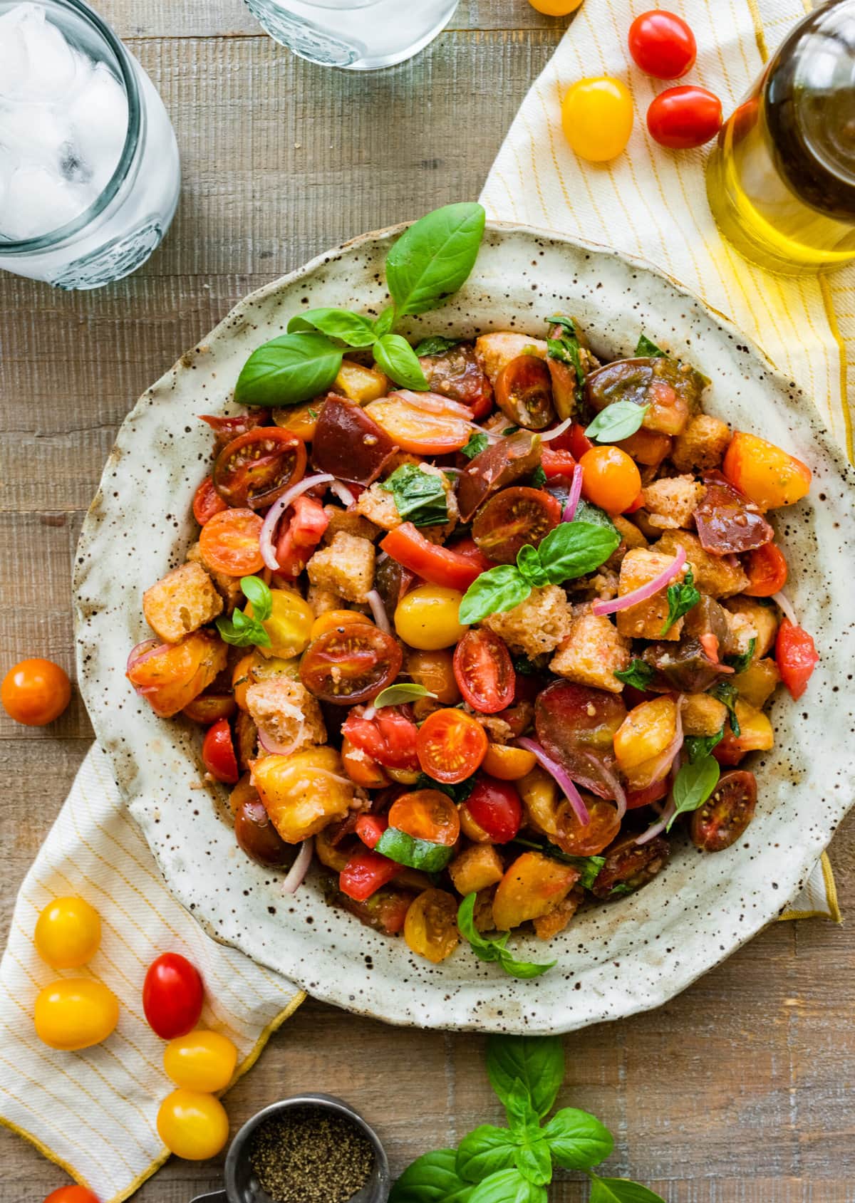 Panzanella salad in a white serving platter with basil as decoration and tomatoes on the side of the plate.