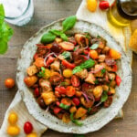 Panzanella salad in a white serving platter with basil as decoration and tomatoes on the side of the plate.
