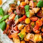 close up of the beautiful summer panzanella salad and all the colors and fresh tomatoes and soaked bread. water glasses and olive oil in the background. side photo.
