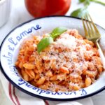 plate of pasta with marinara sauce and fresh tomatoes. for on the side. Tomatoes and basil in background.
