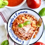 plate of pasta with marinara sauce and fresh tomatoes. for on the side. Tomatoes and basil in background.