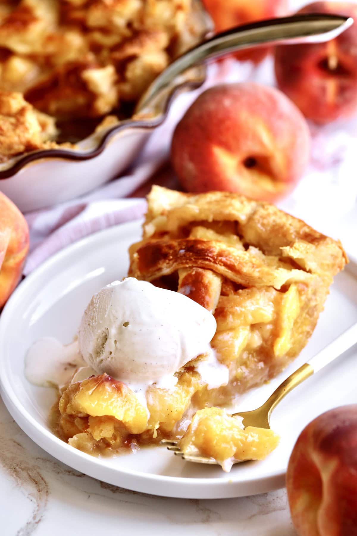 slice of the perfect peach pie on a plate with a fork. Ice cream on top of the slice melting slightly.