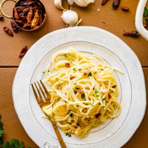 Spaghetti aglio e olio on a white plate with a golden fork.