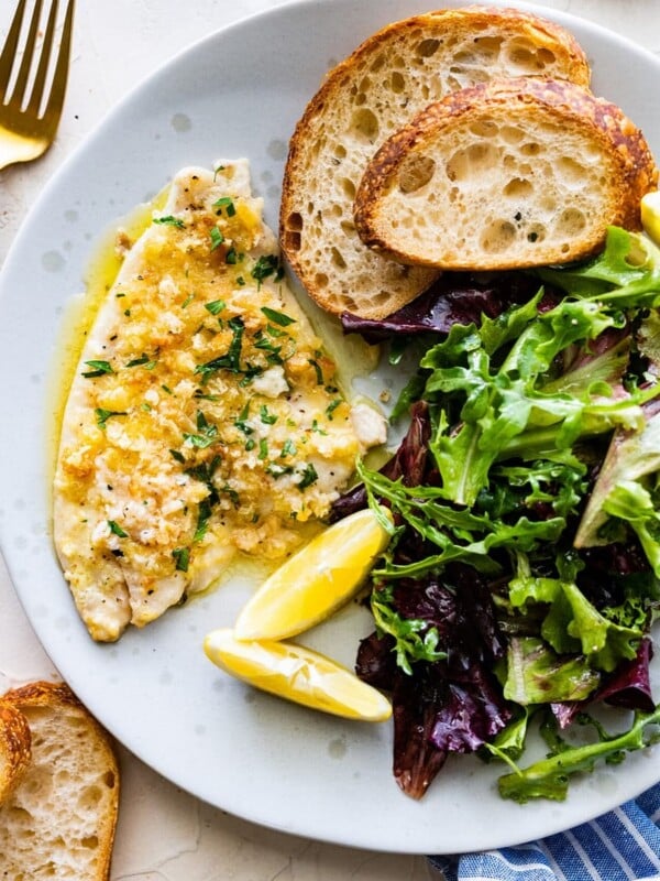Baked flounder on a plate with an arugula salad and crusty bread