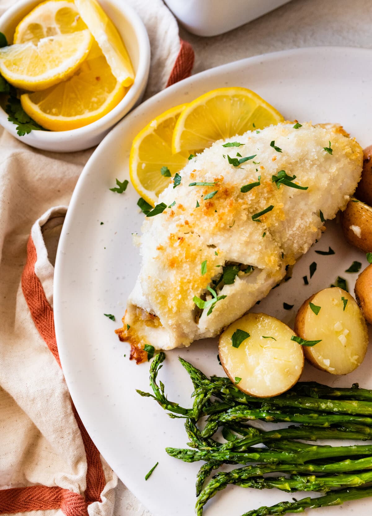 baked stuffed flounder on a plate with lemon wedges. potatoes and asparagus on a plate.
