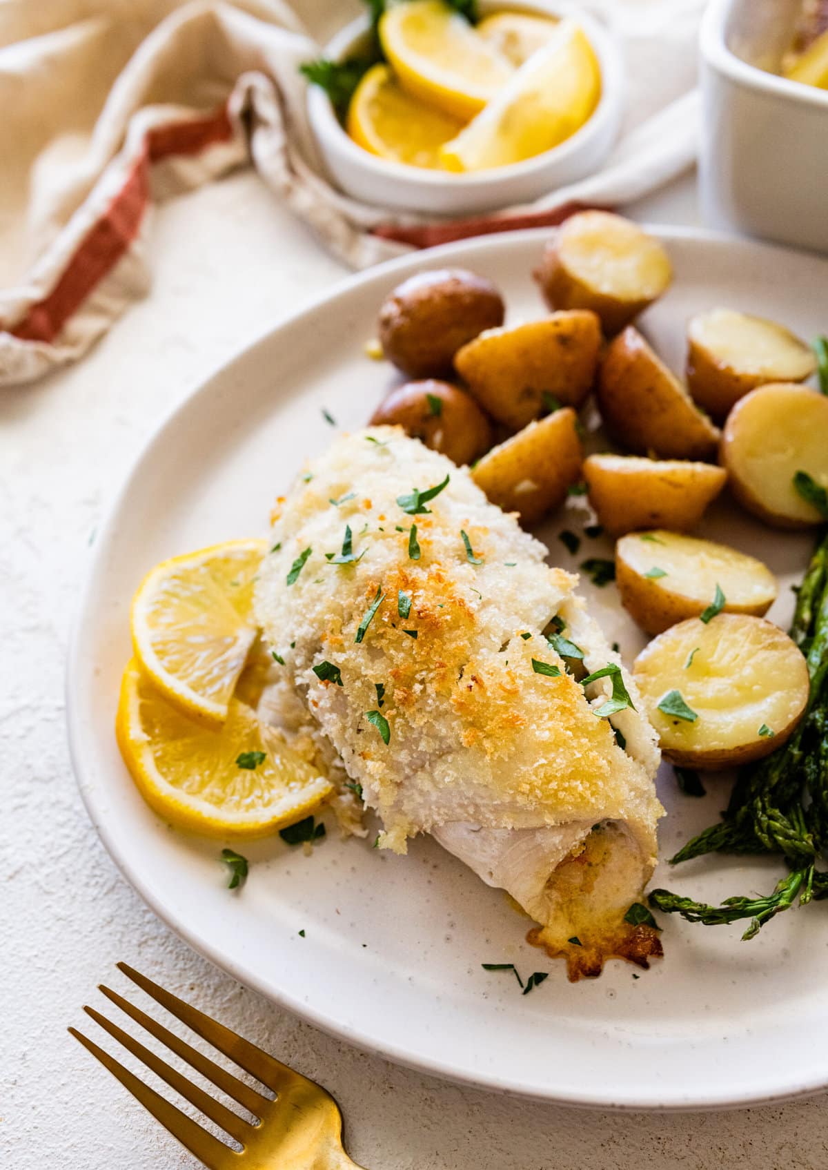 baked stuffed flounder on a plate with lemon wedges. potatoes and asparagus on a plate.