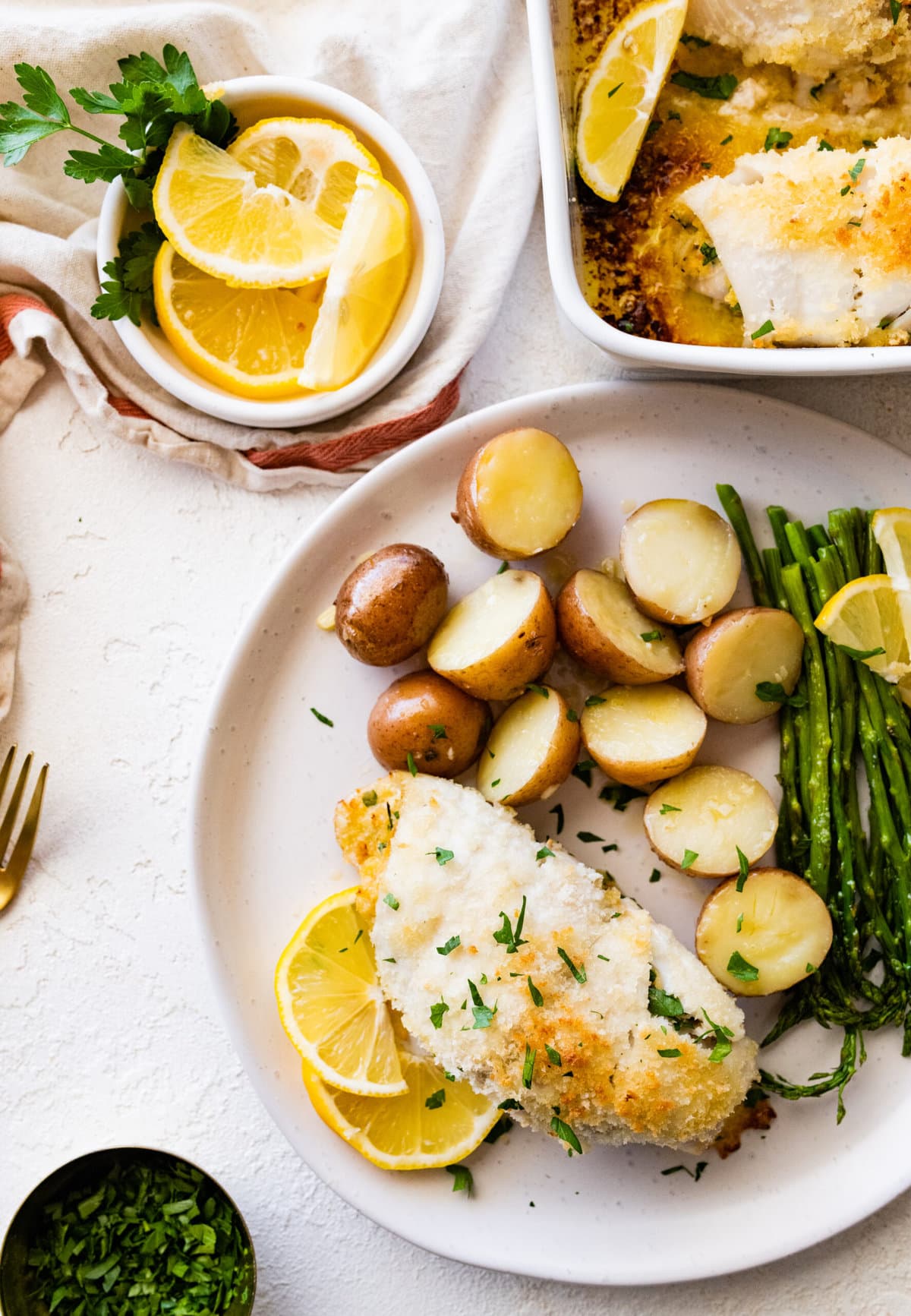 baked stuffed flounder on a plate with lemon wedges. potatoes and asparagus on a plate.