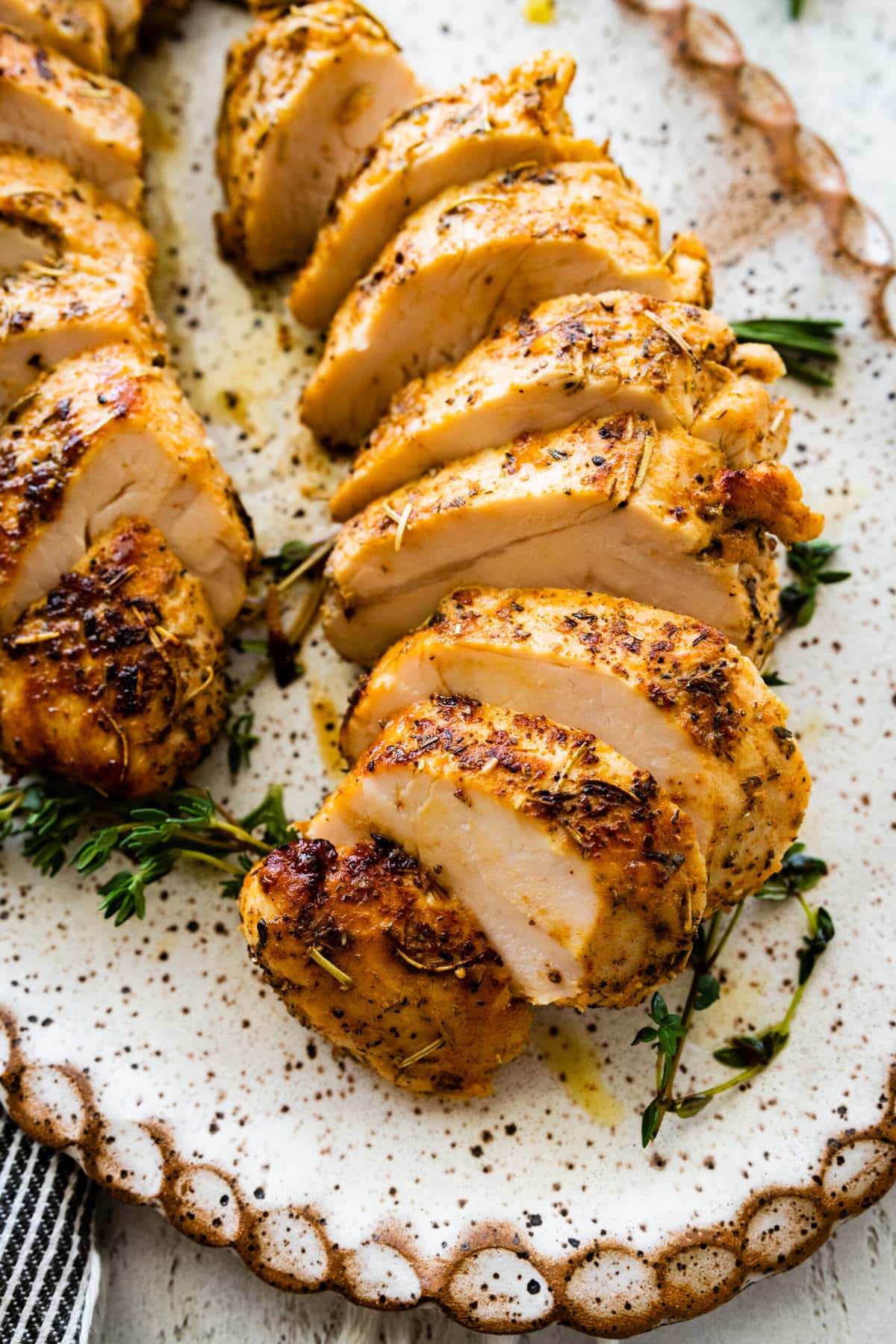 Baked Turkey tenderloin cut into slices on a platter with herbs all around it.