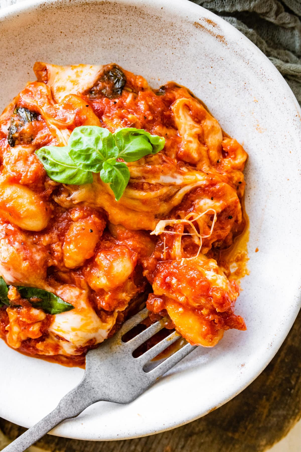 close up of bowl with best gnocchi alla sorrentina. basil leaf and fork in bowl.