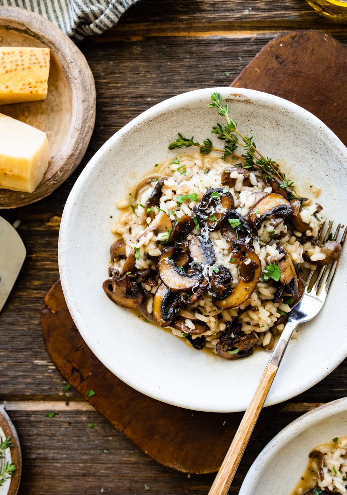 plated mushroom risotto in a white bowl on a wooden board background.