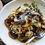 close up of plated mushroom risotto in a white bowl with a fork in the bowl.