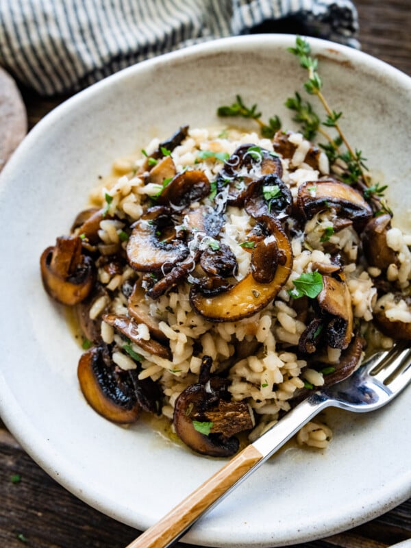 close up of plated mushroom risotto in a white bowl with a fork in the bowl.