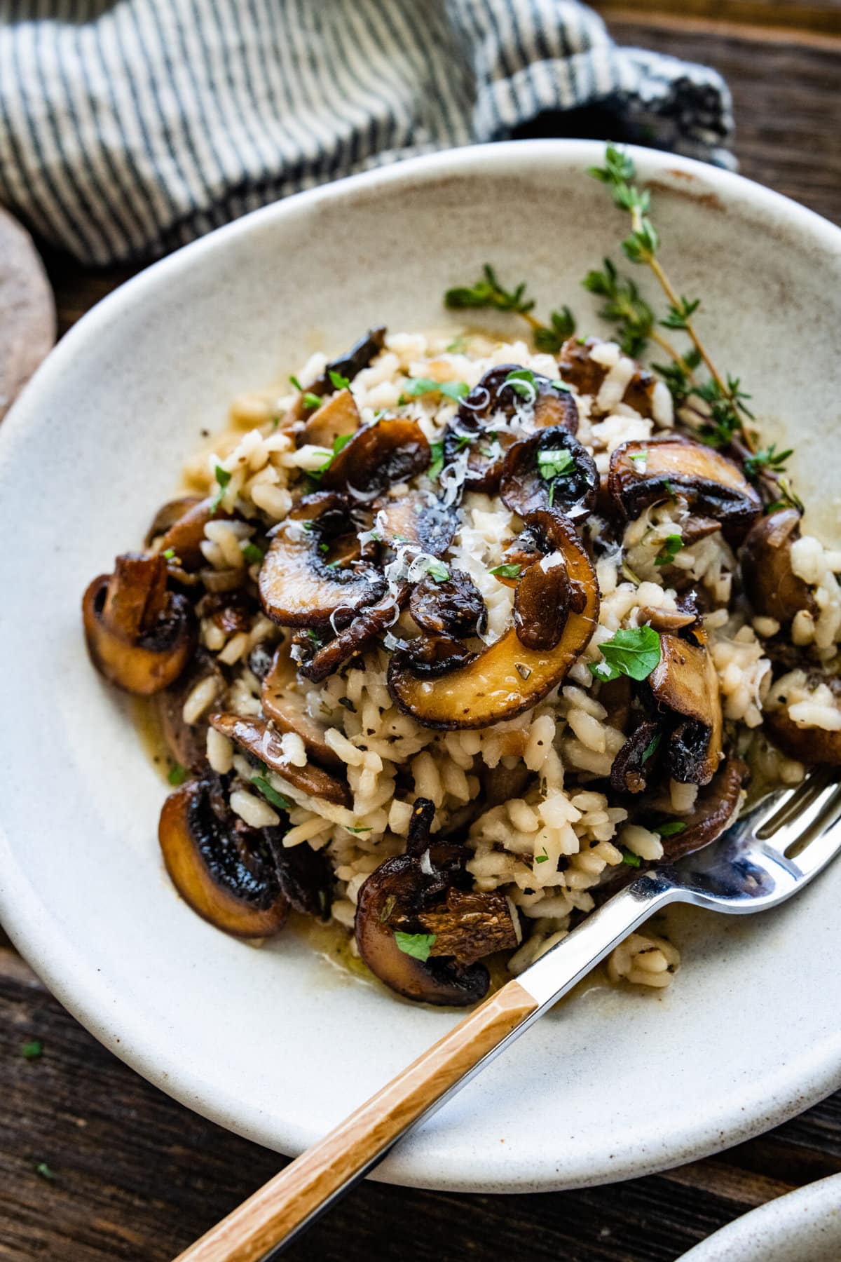 close up of plated mushroom risotto in a white bowl with a fork in the bowl.