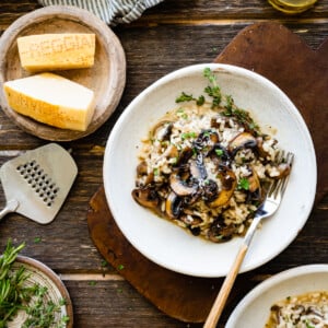 plated mushroom risotto in a white bowl on a wooden board background.