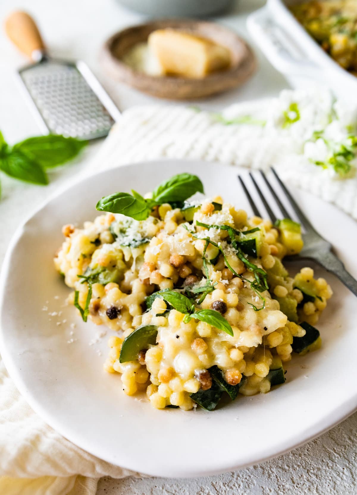 finished Fregola Sarda Pasta Recipe with Zucchini and Cheese in pan. Up close shot on a white plate with a fork.