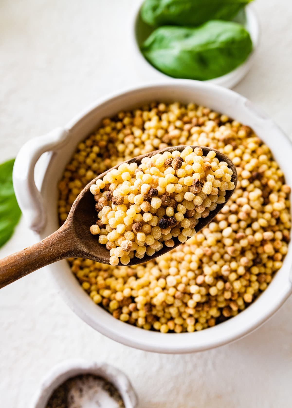 close up of fregola sarda in a wooden spoon.