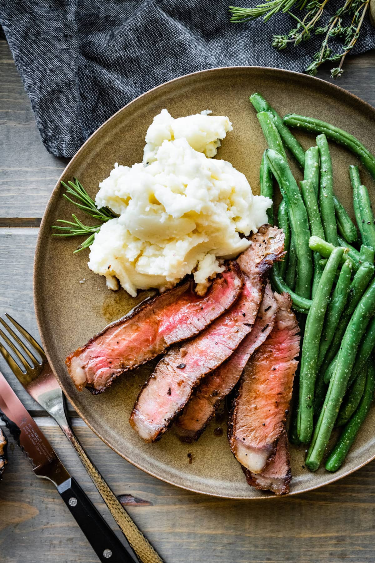 T-Bone Steak on a plate with mashed potatoes and green beans. Fork and knife and napkin.