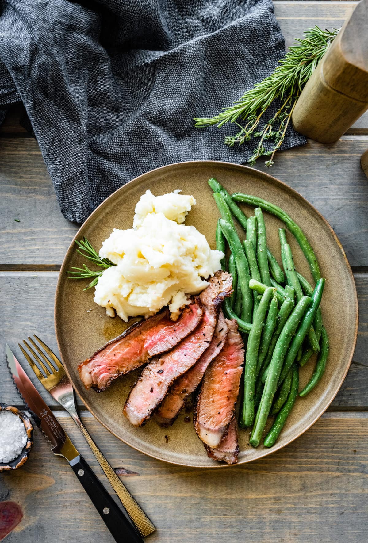 T-Bone Steak on a plate with mashed potatoes and green beans. Fork and knife and napkin.